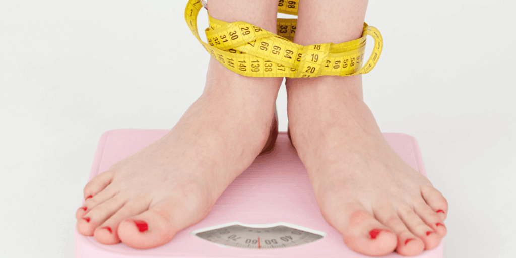 Female body standards depicted through feet on a scale with measuring tape
